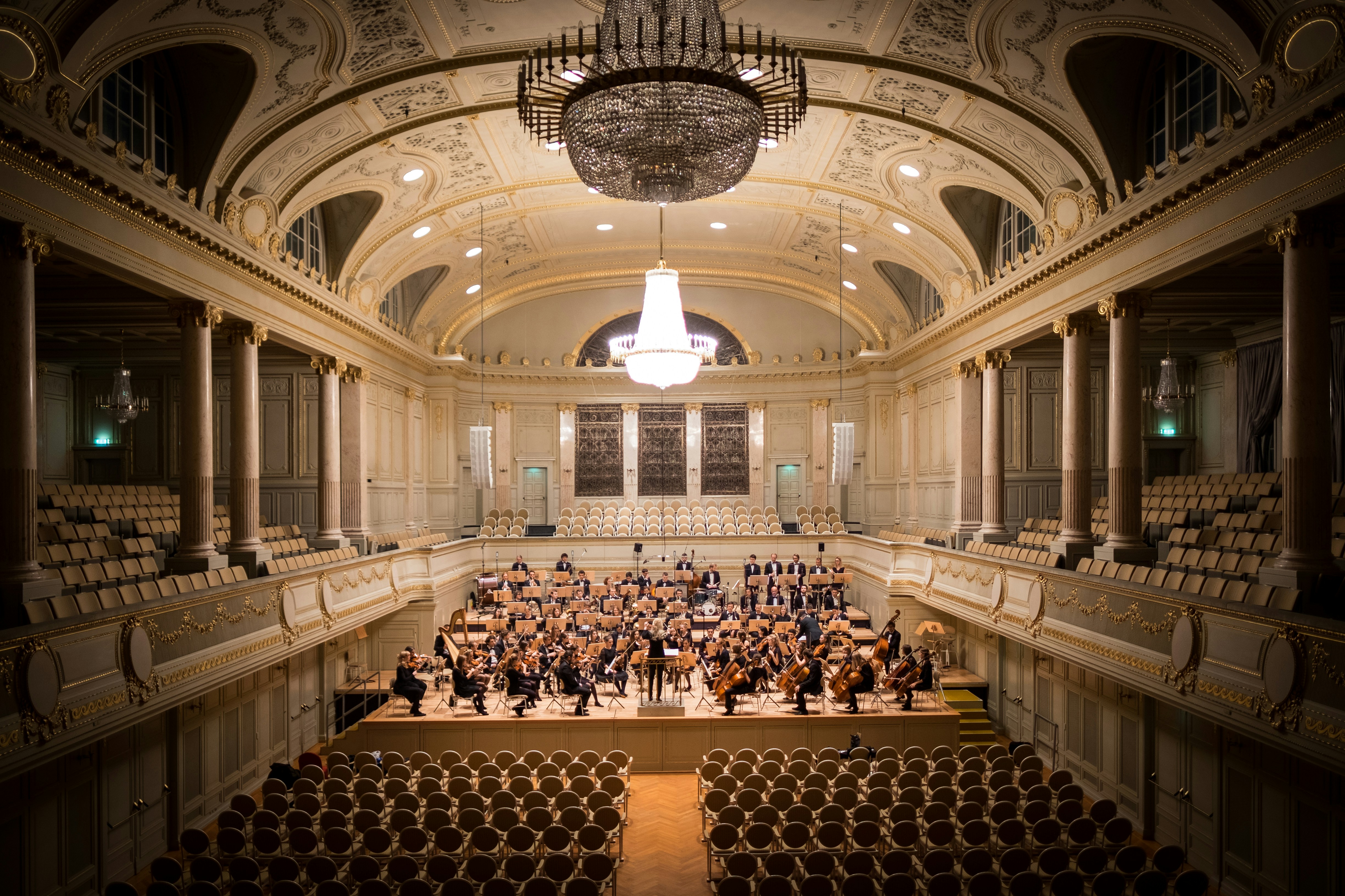 Orchestra performing in an elegant concert hall with ornate architecture and crystal chandeliers